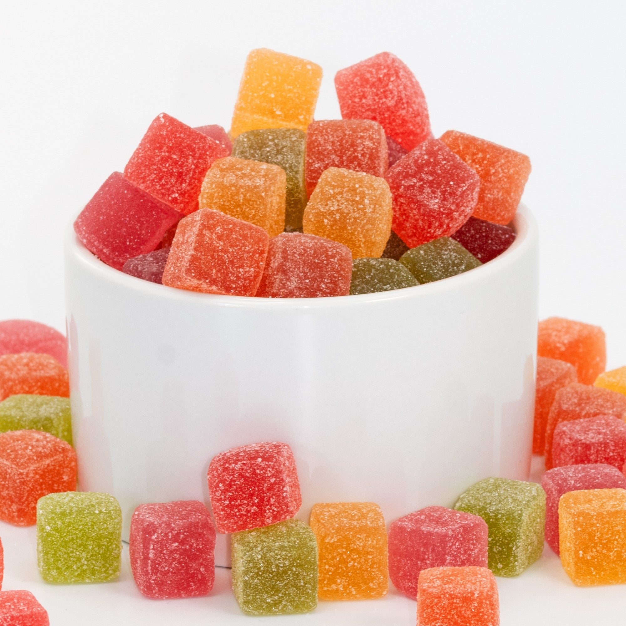 Colorful gummy cubes in a white bowl on a white background